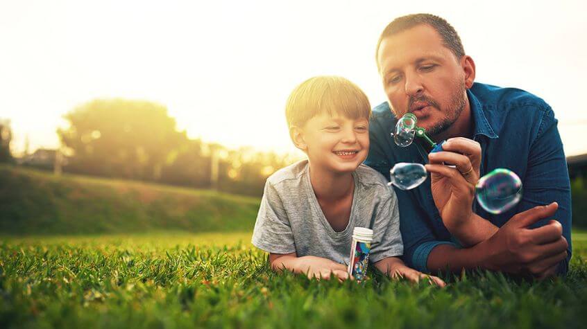 Father and son blowing bubble on the lawn maintained with landscaping supplies